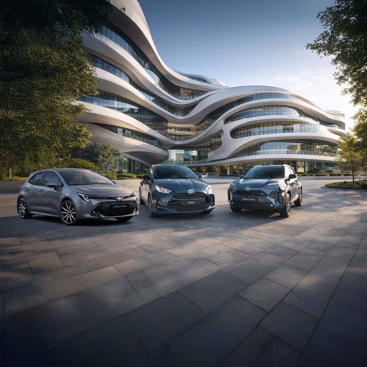 Ein Toyota Yaris und ein Toyota Yaris Cross stehen nebeneinander auf einem gepflasterten Platz vor modernen, terrassenförmig angeordneten Wohngebäuden bei Abendlicht.